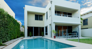 Two storey Airbnb property with a pool and a glass fence in the back yard, lined by a green hedge