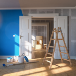 A ladder stands in the foreground of a half painted blue room, with painting equipment ready to finish the job. Painting is usually claimed as an improvement and is depreciated over 40 years.