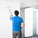 A person in a blue shirt paints a wall in an investment property. Painting is an example of an improvement in depreciation terms.