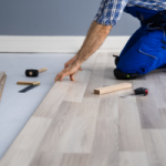 Person laying new floor in an investment property. This is an example of an improvement that needs to be added to a depreciation schedule so depreciation can be claimed.