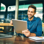 A client in a blue shirt sitting at a cafe reading Depreciator's News on their tablet